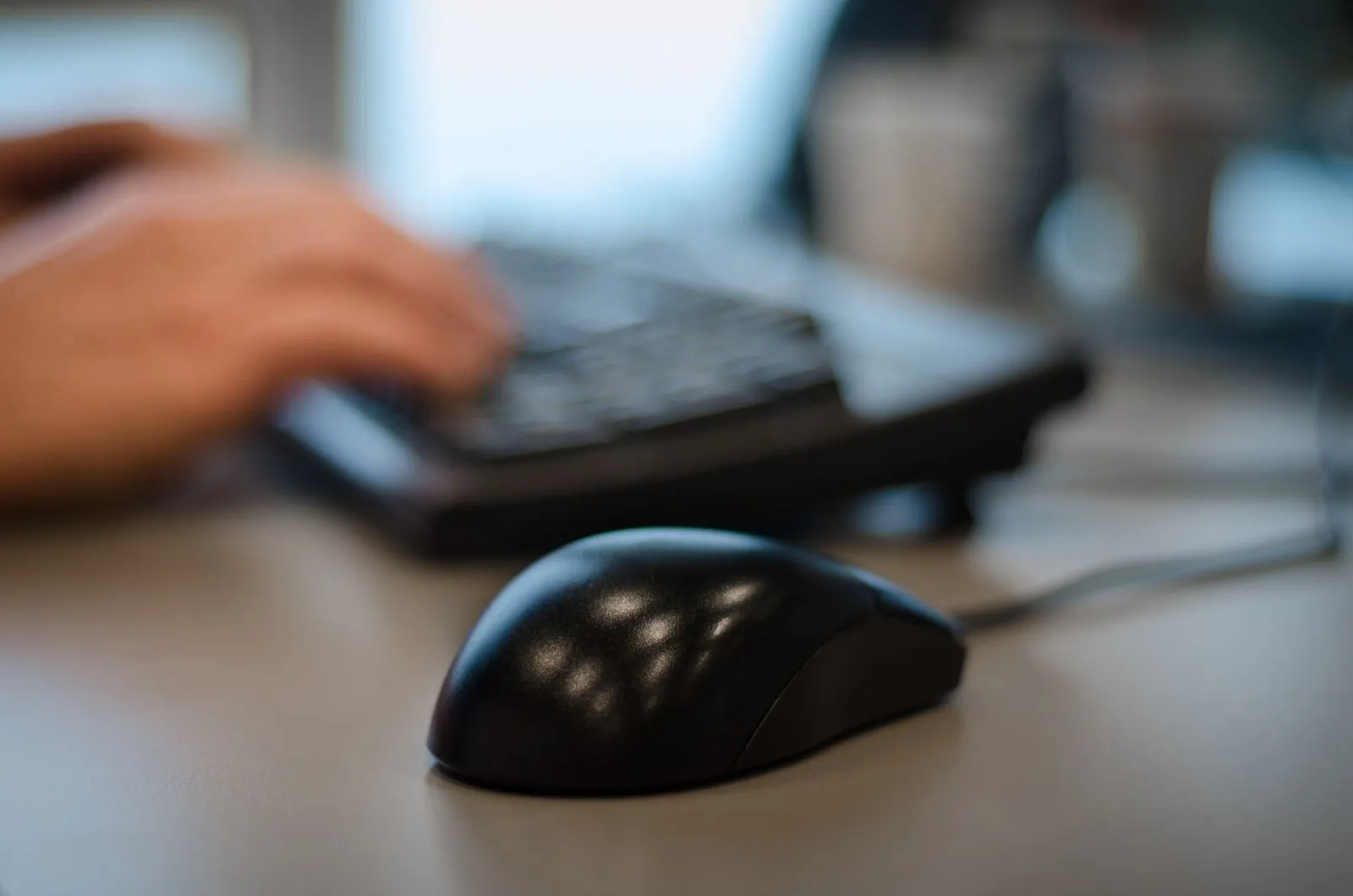 Blurry background with a focus on a computer mouse in an office setting.